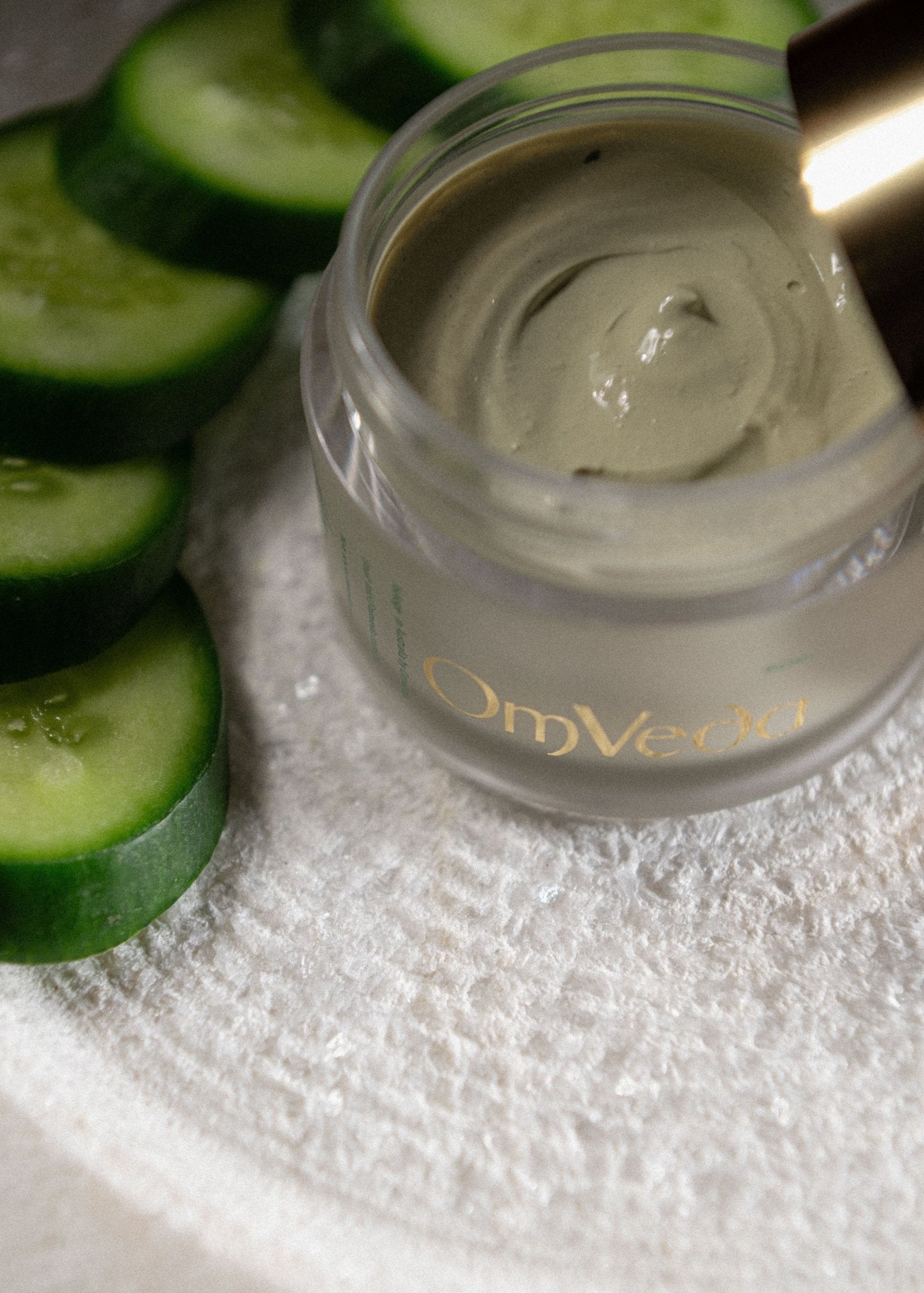 OmVeda cucumber face mask in glass jar with pale green cream and cucumber slices