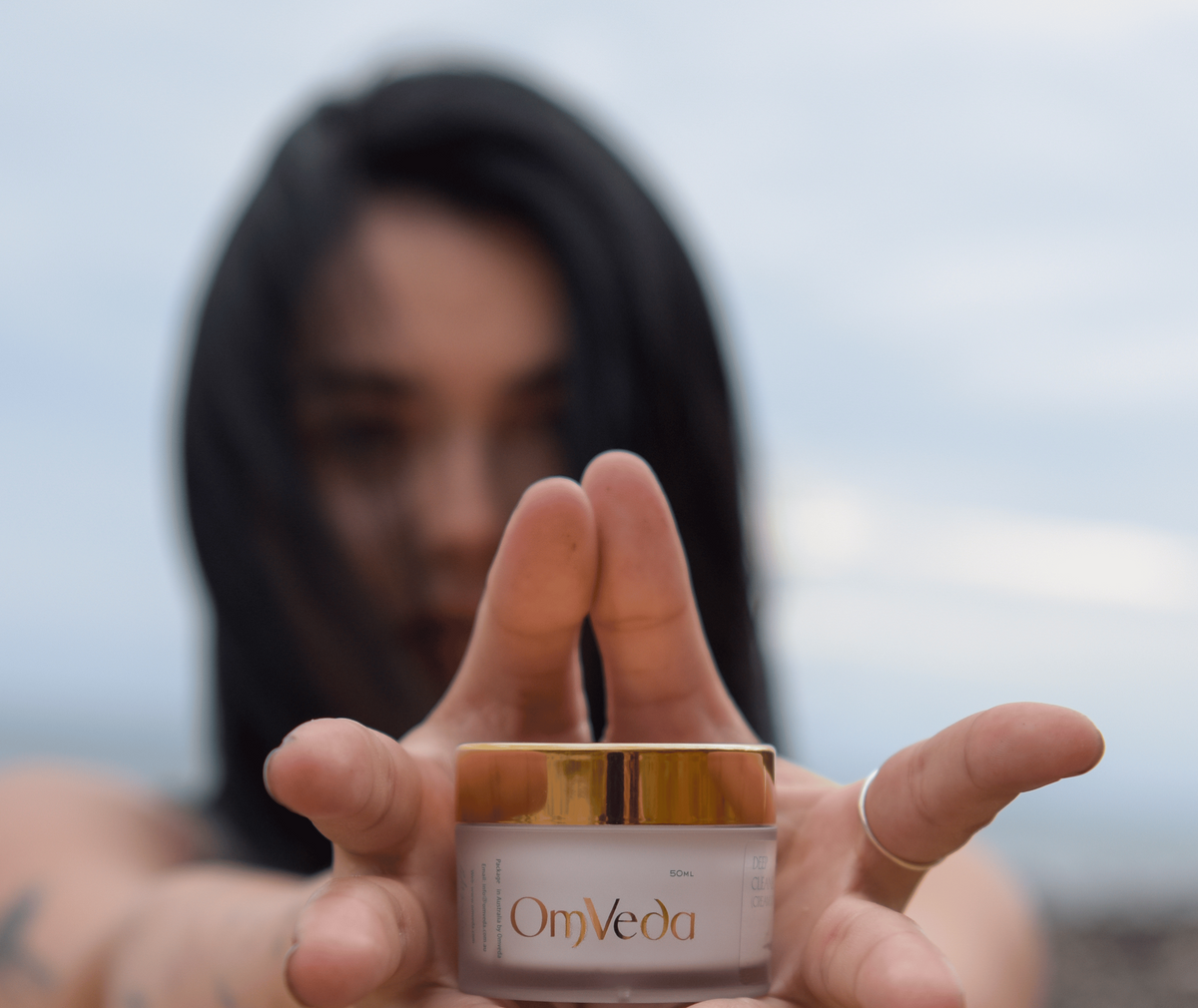Woman holding out a jar of OmVeda skincare towards the camera