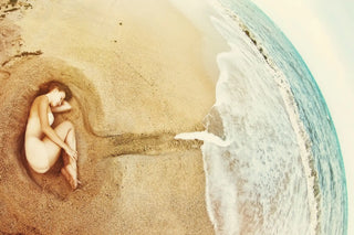 A human ear carved or sculpted in beach sand near ocean waves.