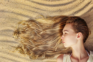 Long blonde hair flowing across sand in a side profile view.