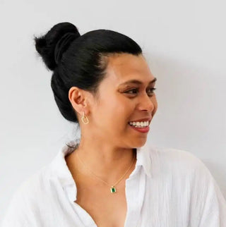 A smiling person wearing a white button-up shirt and gold jewelry.